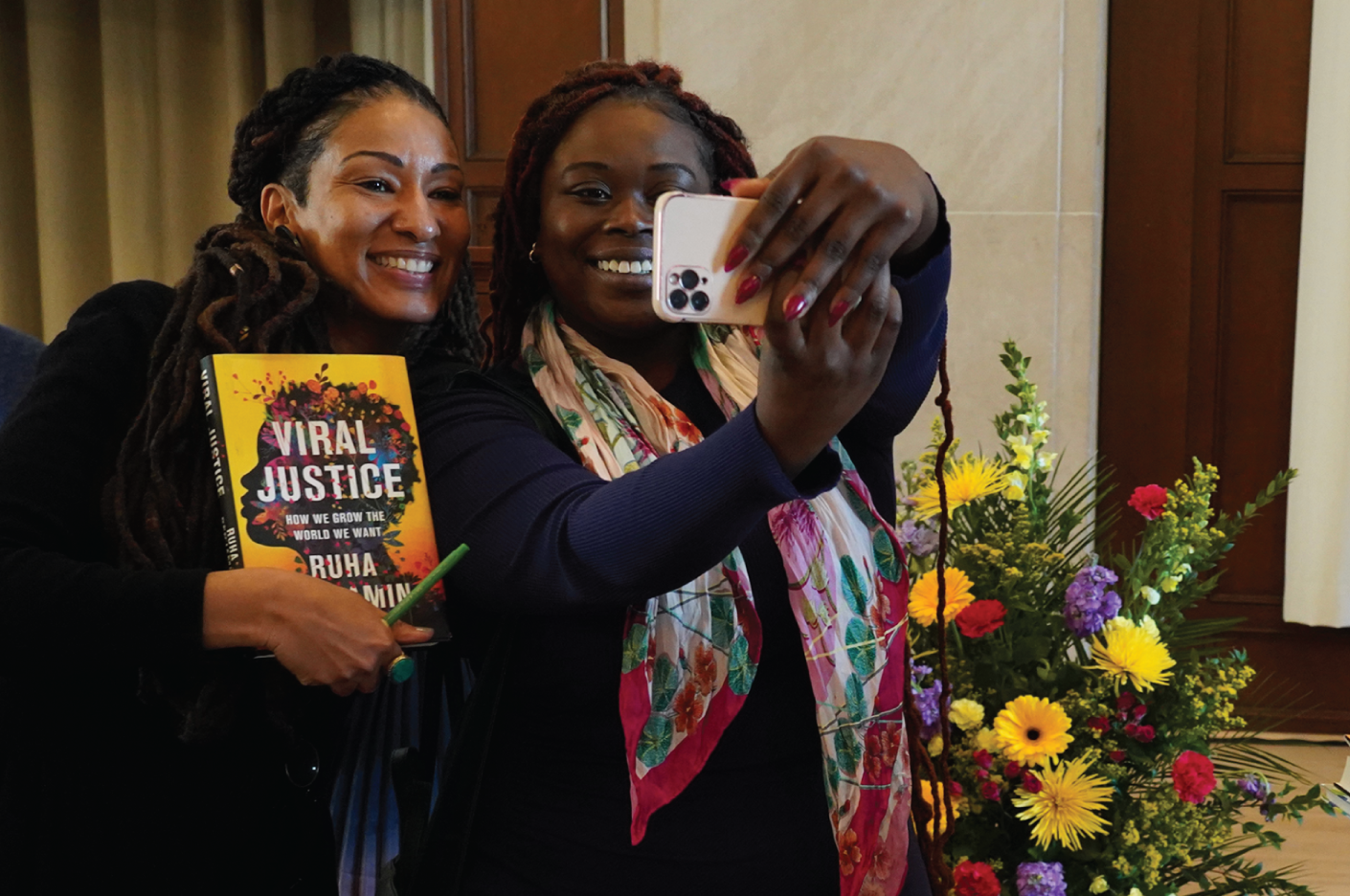 Two people take a selfie. One is holding the book Viral Justice.