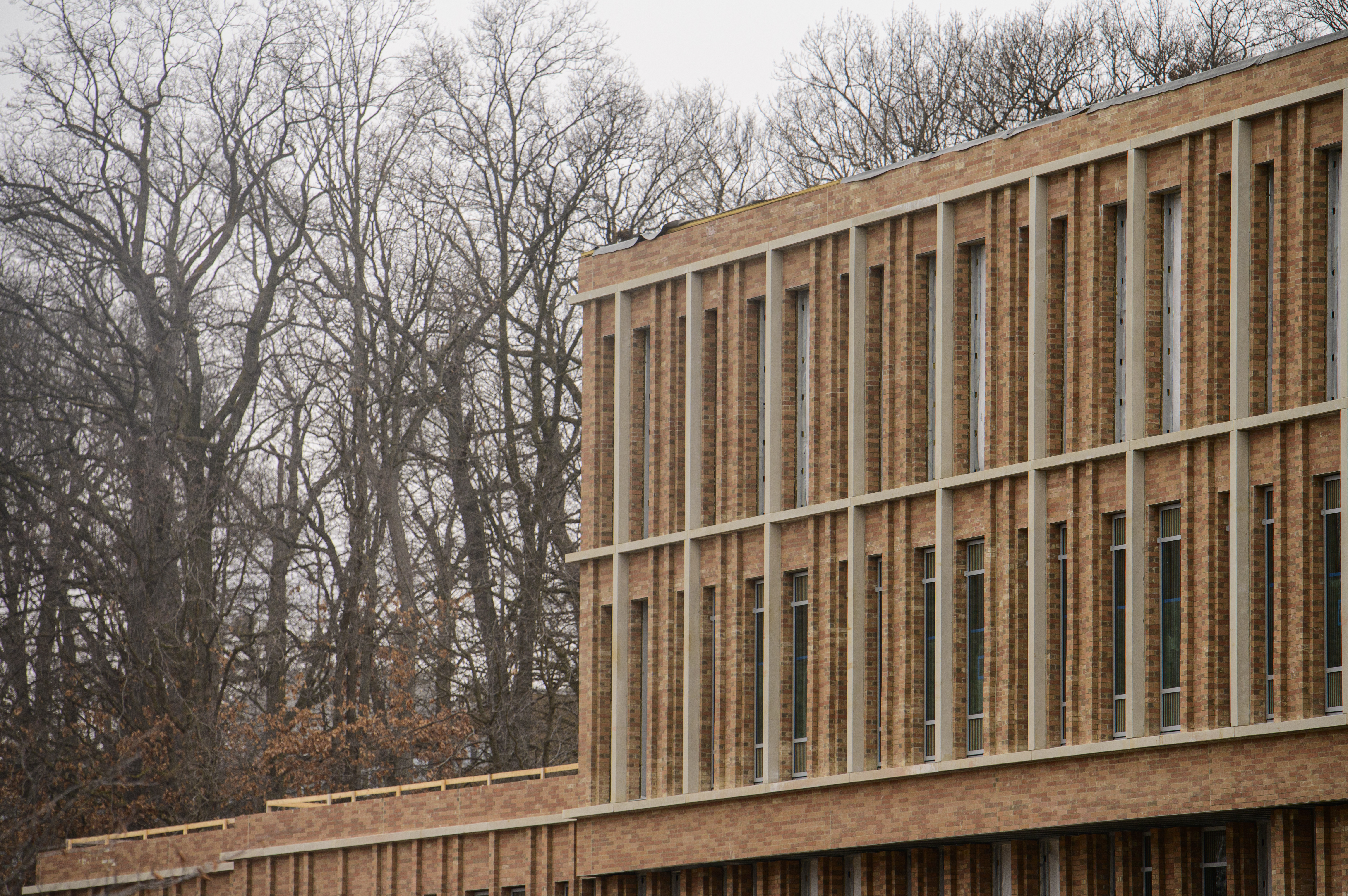A brick building with vertical lines of windows and a forest in the distance