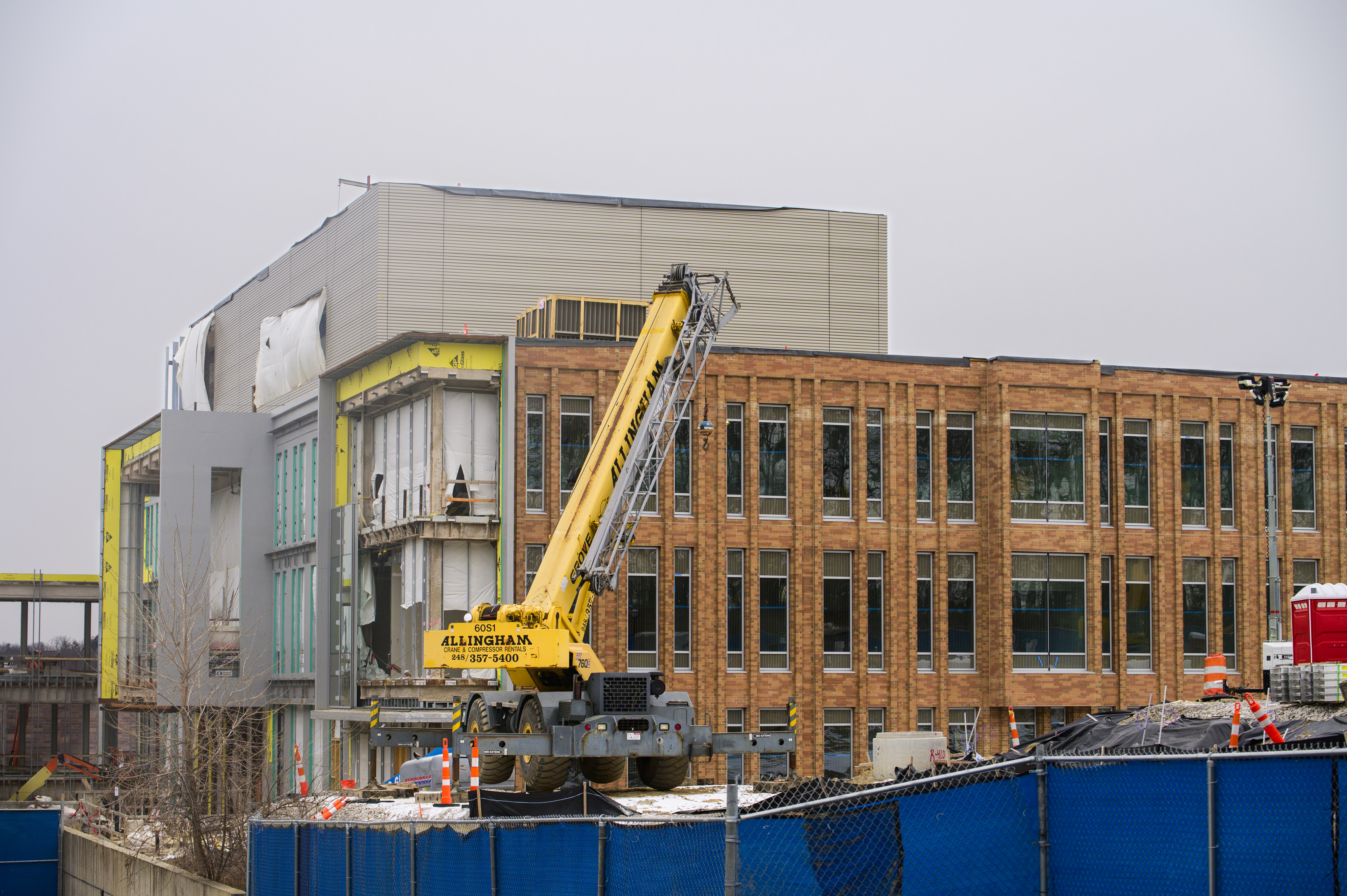 A brick facade with long narrow windows is under construction, with a large crane in the foreground.