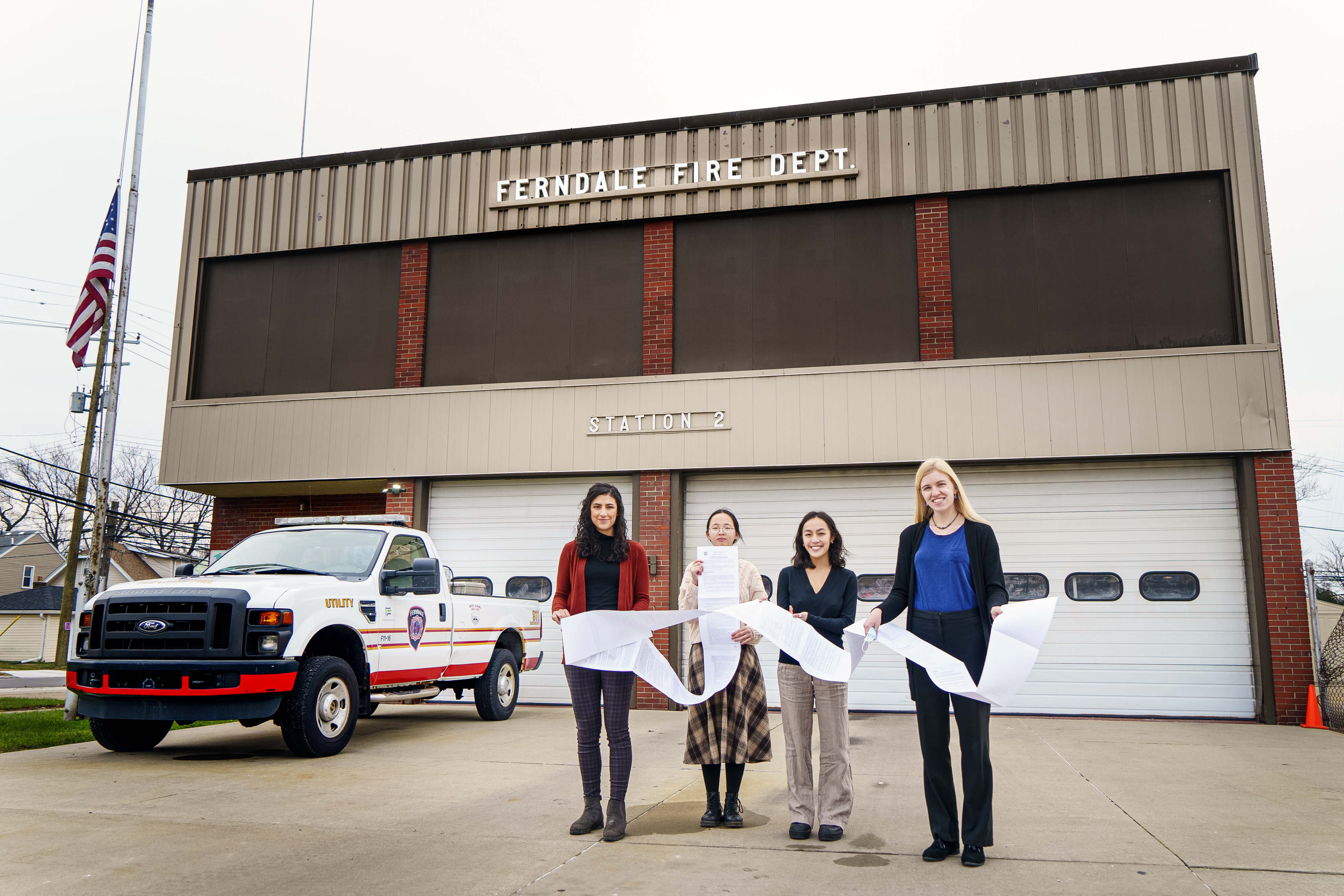 Four students hold a long document in front of a fire station in ferndale