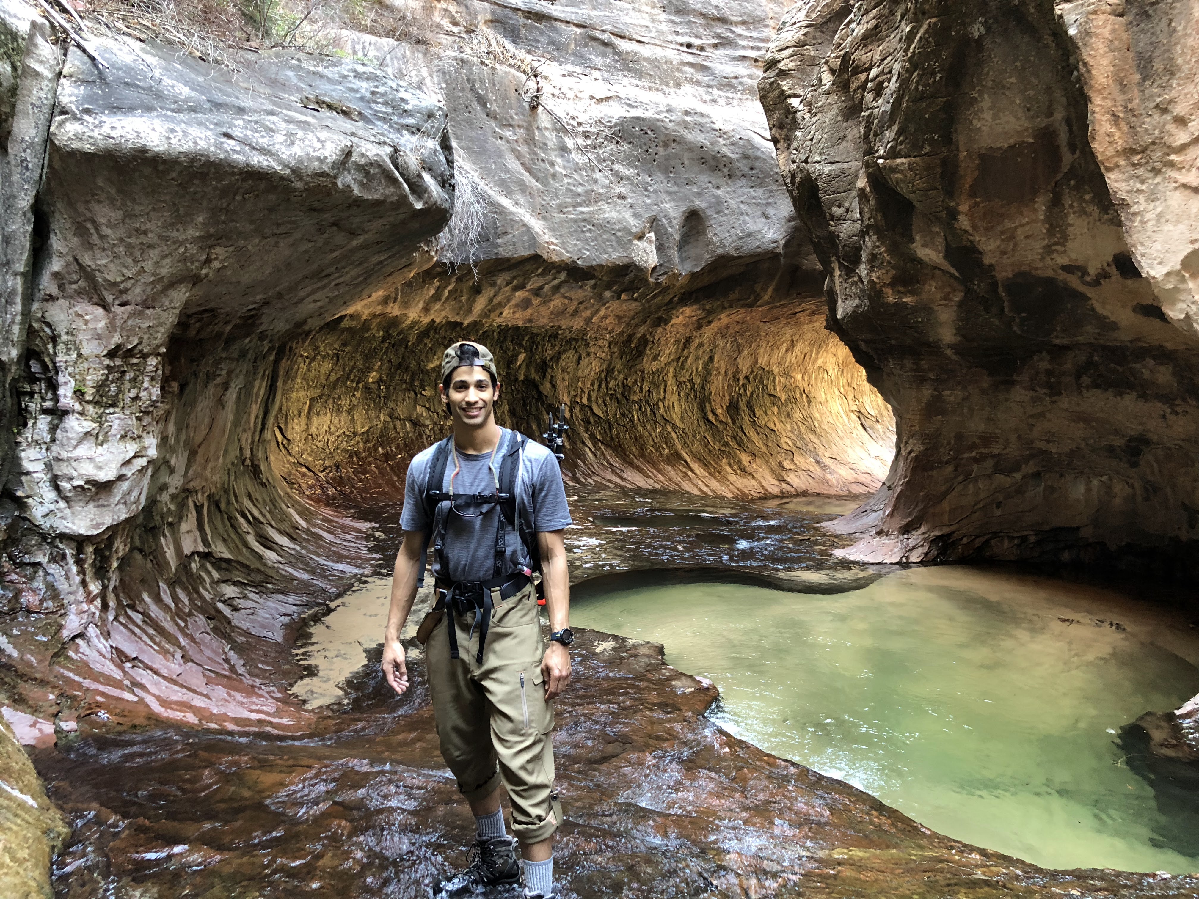 Ermias wears waders and stands in a stream in a rocky canyon