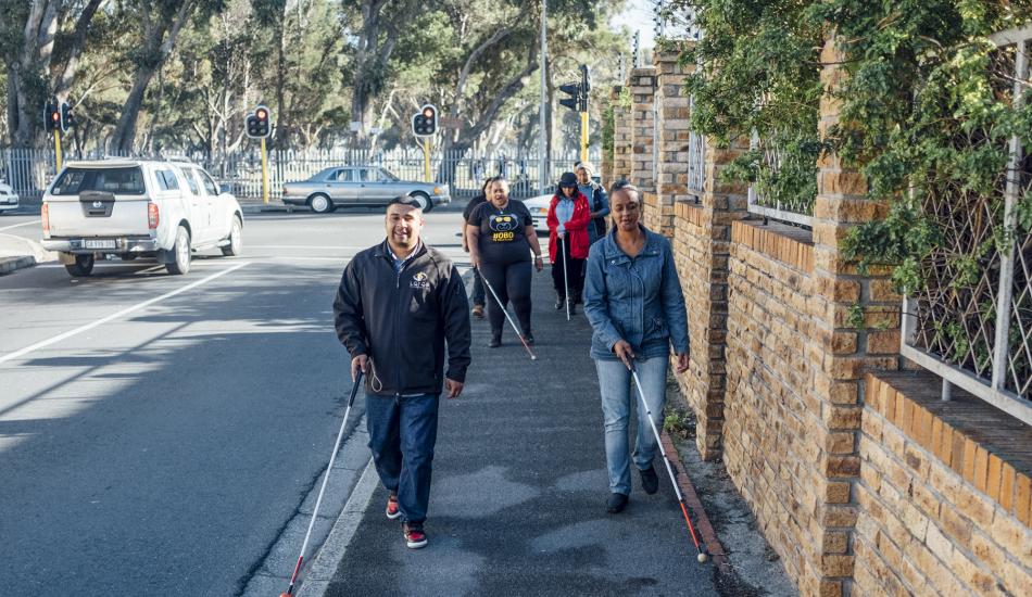 A group of people walking down a sidewalk using canes