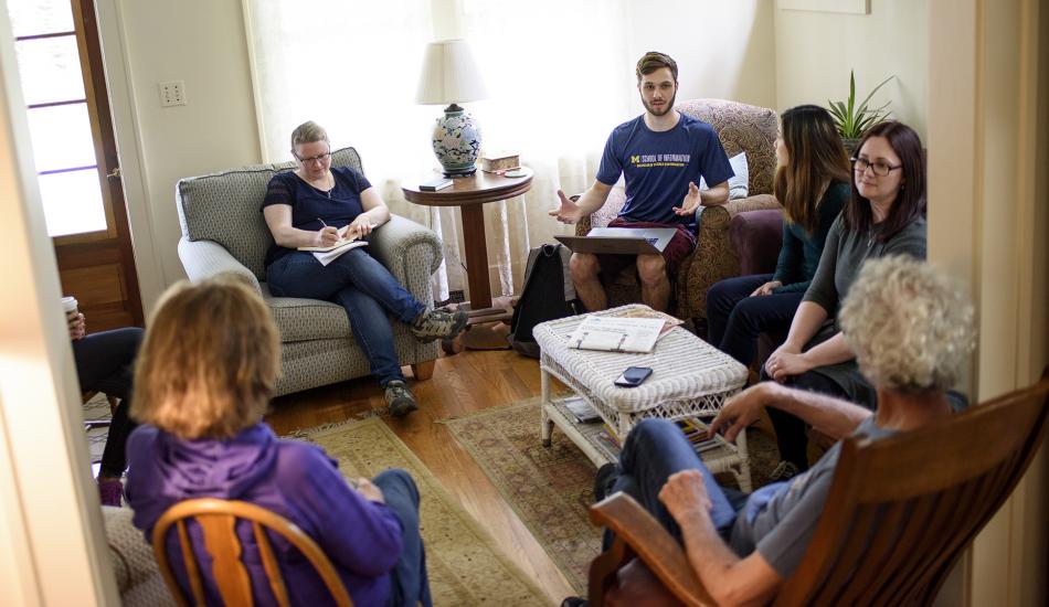 Students and community members talking in a living room.