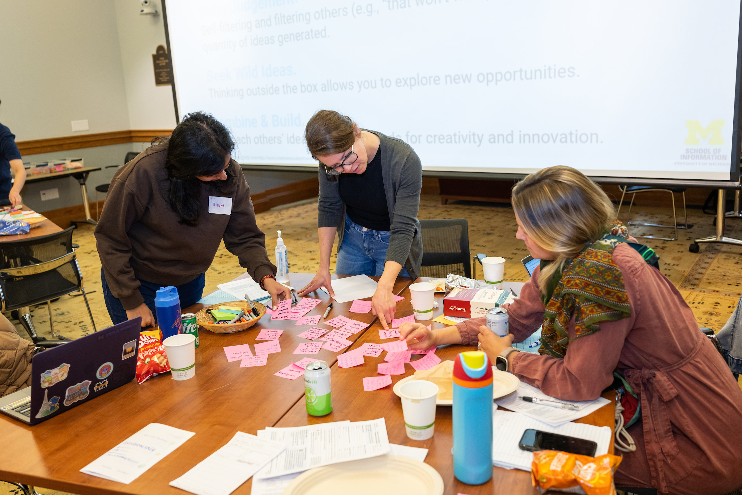 Rachael Zuppke stands at a table covered in Post-It notes, chatting with two other workshop participants