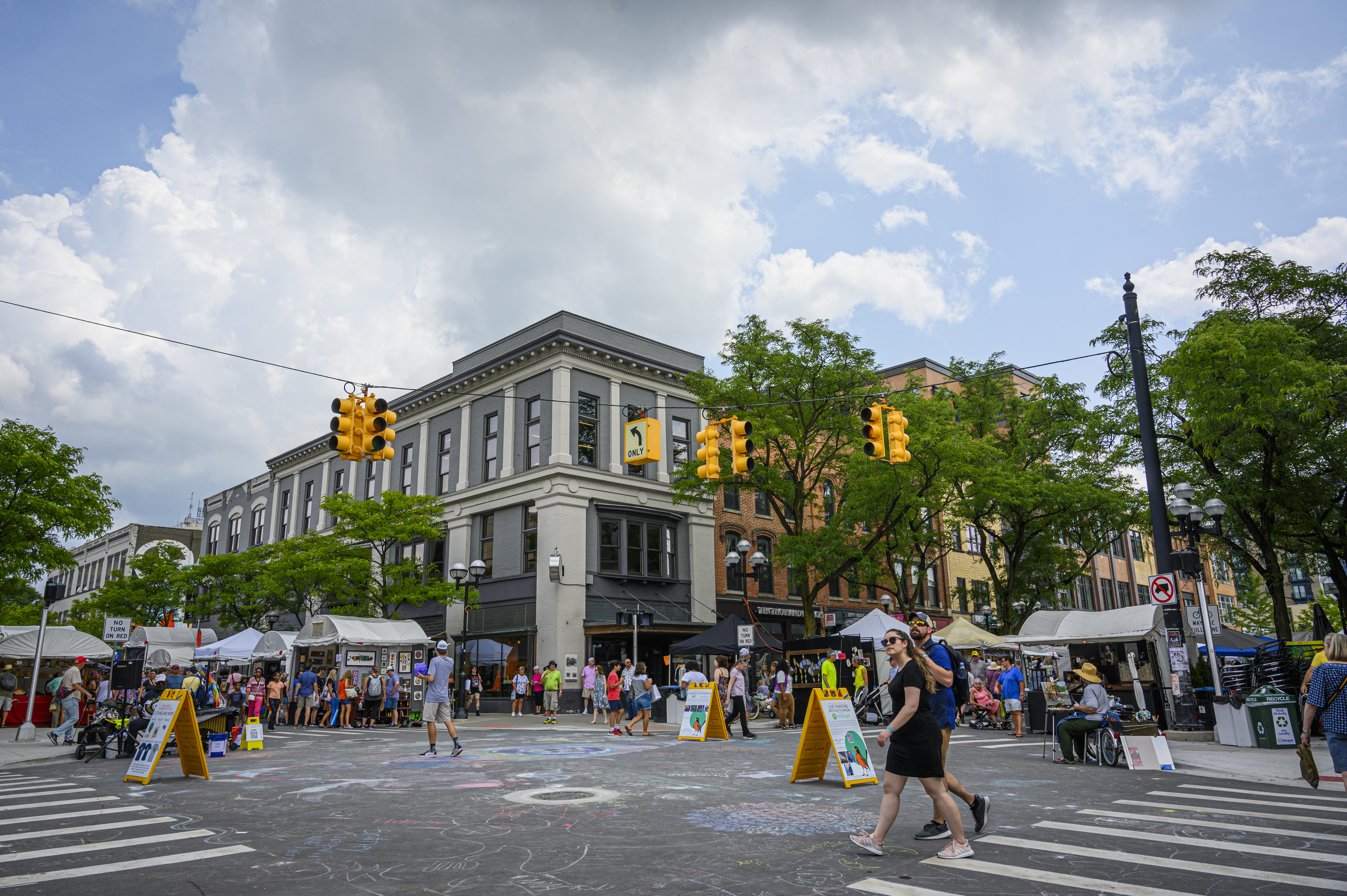 Downtown Ann Arbor during a street fair. There are tents lining the streets and chalk art on the ground.