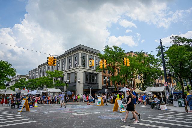 Downtown Ann Arbor during a street fair. There are tents lining the streets and chalk art on the ground.