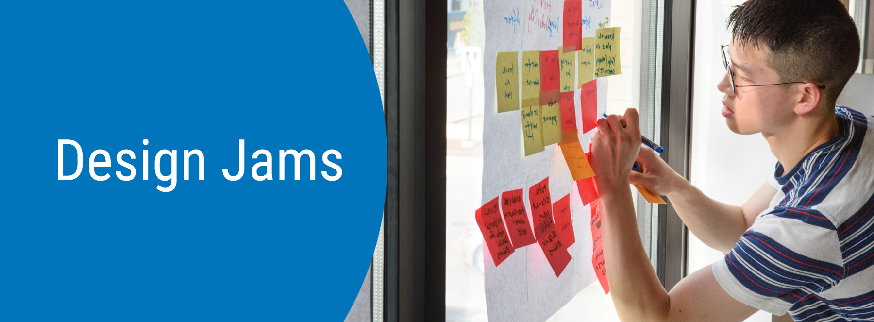 Design Jams. A student writing on a sticky note grouped with other notes on a wall.