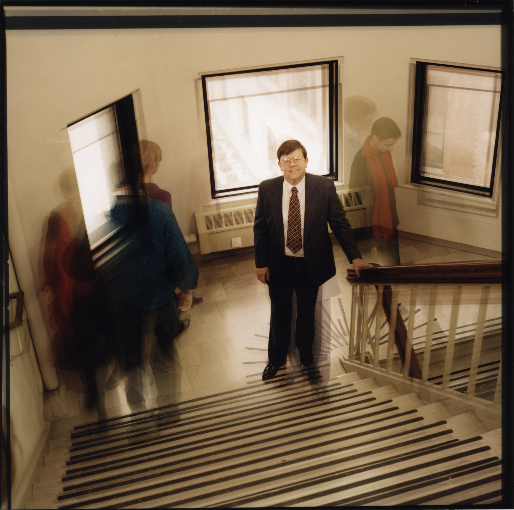 A film photography of Daniel Atkins on a staircase, with other people walking past.