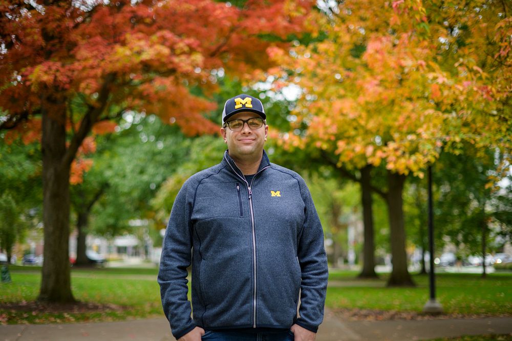 Kyle Bylin stands on the U-M campus with fall foliage in the background.
