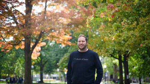 A photo of Joey Quick standing on campus with fall foliage behind him.