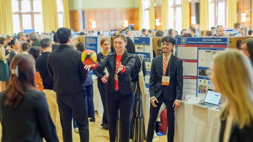 Students standing in front of a trifold display in the ballroom of the Michigan League toss around a rugby ball