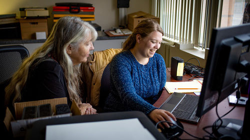 Two people sitting at a desktop computer together.