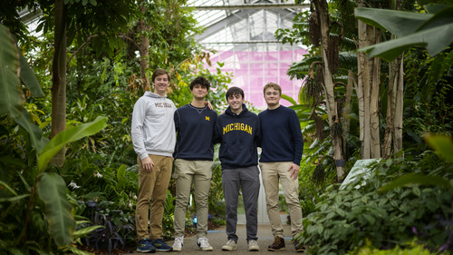 Four students standing in a green house surrounded by trees and plants.