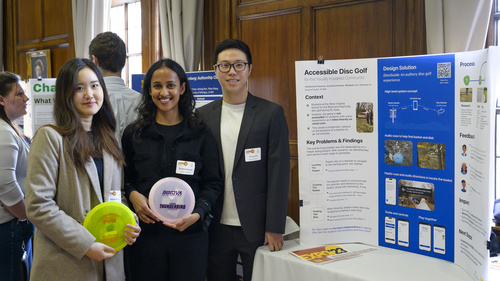 Three students standing next to a tri-fold poster titled "Accessible Disc Golf." Two of them are holding discs