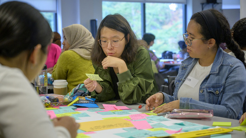 Three students writing on and arranging sticky notes on a table.