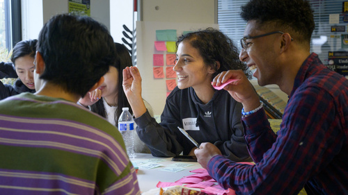 Students talking together at a table covered in sticky notes.