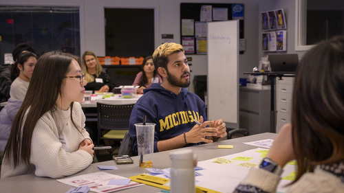 Three students talking together at a table with sticky notes on it