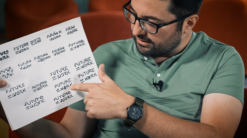 Pedro Pazmino holds up a sheet of paper covered in hand drawn early versions of his Future of Work logo. He points to one.