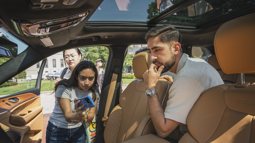 An interior view of a vehicle as three UMSI students study the user interface, with one taking a photo on their cell phone