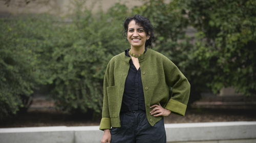 Amina Abdu smiles into the camera while standing outside wearing a green cardigan. 