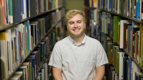 Austin Book poses in the library stacks with books on either side of him