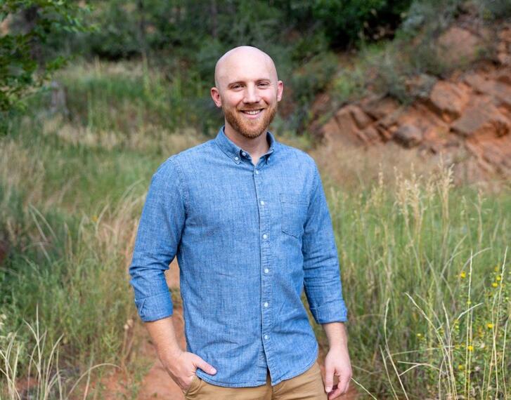 Dane Jacobsen smiling outdoors in a grassy landscape featuring craggy rock face.