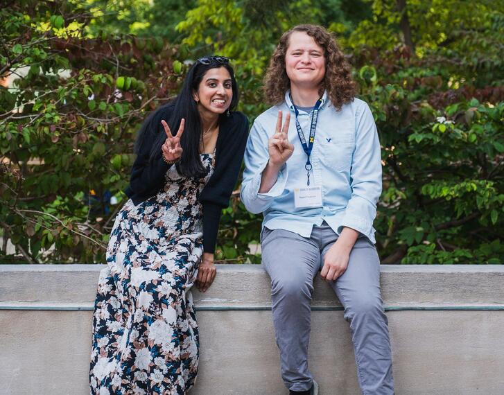 Students sit on a bench on the U-M campus and are smiling.