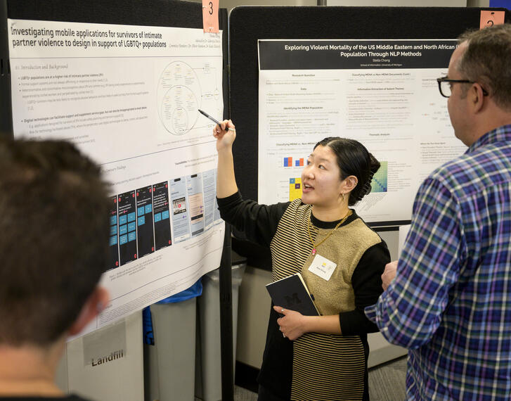 Students gather in a small event room lined with research posters on either side.