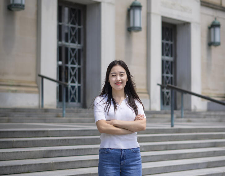Jane Im stands in front of an academic building, arms crossed in front of her 
