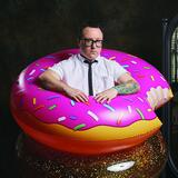 A headshot of Paul Woods in an inflatable donut with pink icing and sprinkles