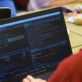A person looking at a laptop screen. There are four different windows open on the screen and they have code on them.