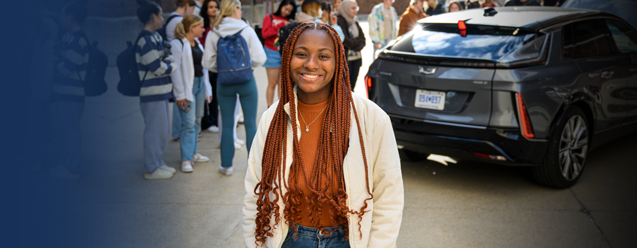 Briarre stands in front of an SUV and a group of students who are looking at it.