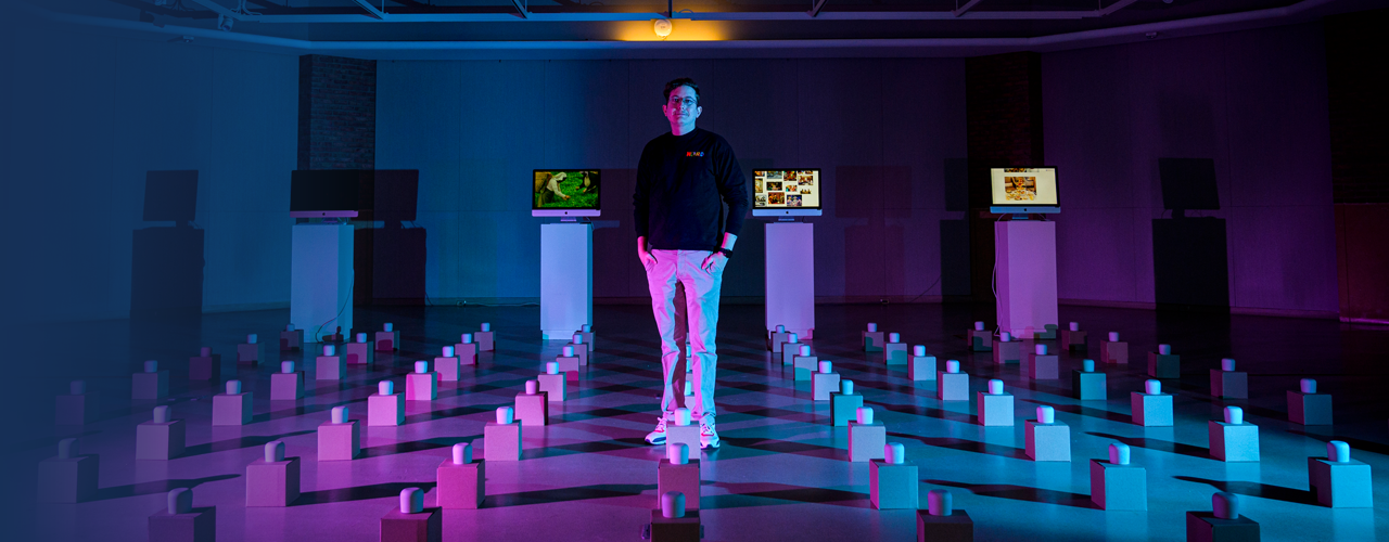 Josh among an art exhibit of many tea cups on boxes laid out in a grid pattern across the floor.