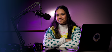 A student sitting at a desk with a laptop and a microphone