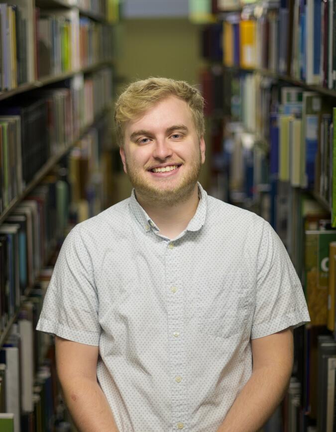 A headshot of Austin Book with library bookshelves in the background.
