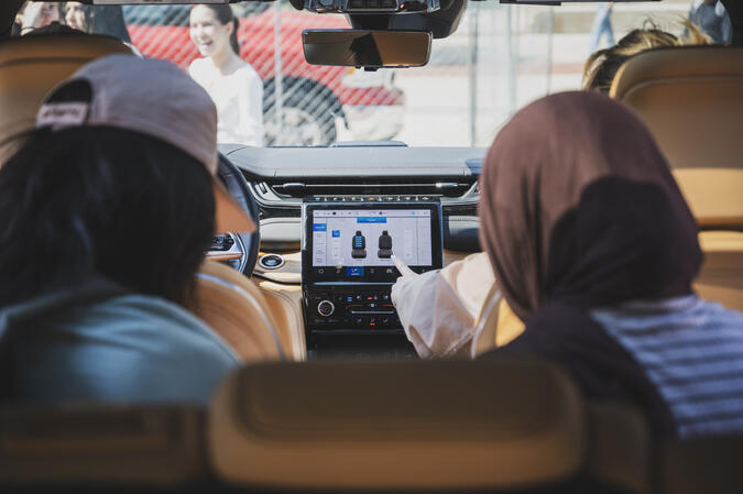 A backseat view of two students looking at the digital dashboard of a new car.