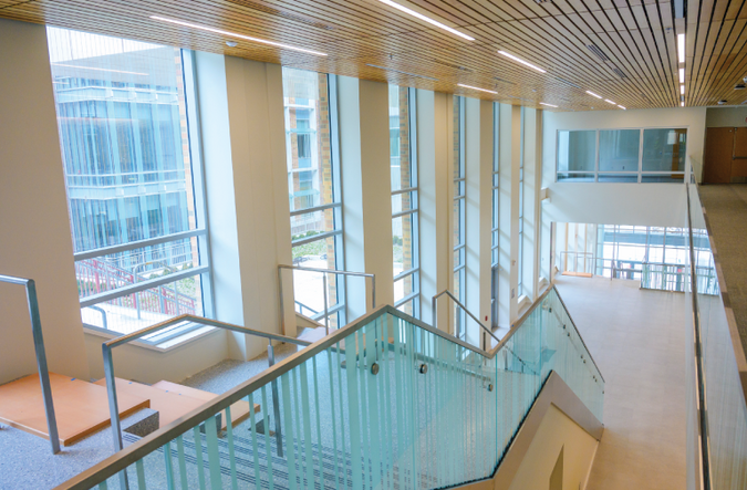 An interior view of a stairway in the Leinweber building. The left wall has large floor to ceiling windows facing the outside.