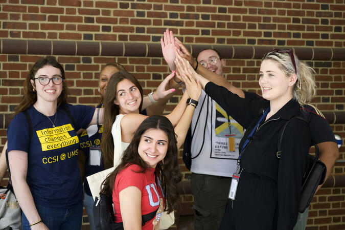 7 people all high-fiving at once. One of the has a shirt that reads, "Information changes everything. CCSI @ UMSI."