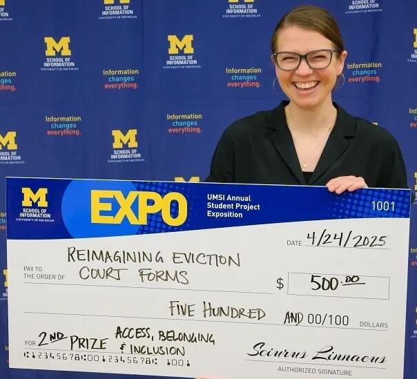 A student holding a giant check made out to Reimagining Eviction Court Forms for $500.