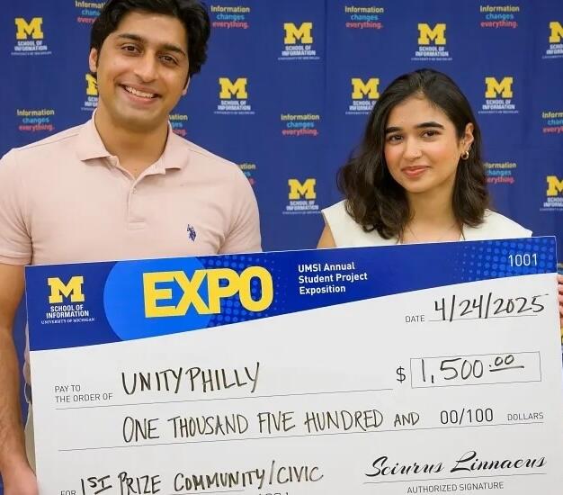 Two students holding a giant check made out to UnityPhilly for $1,500.
