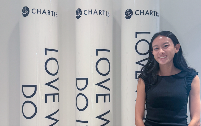 A student standing next to three pillars with the Chartis logo on them.