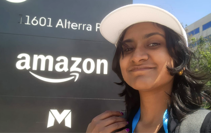 A student standing next to a sign with the Amazon logo on it.