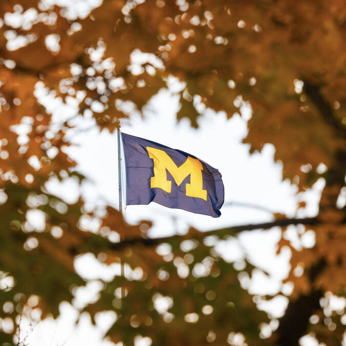 The Michigan Union flag is framed by orange leaves on a nearby tree on a fall day.