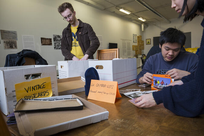 Three students work intently at a table covered in file boxes with different lables
