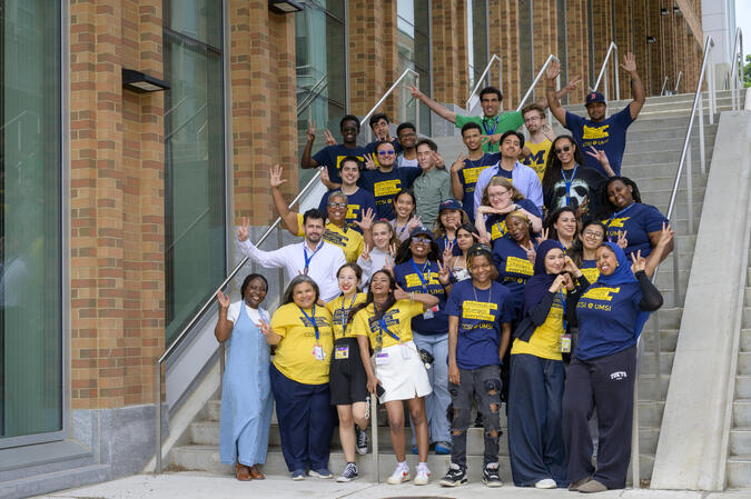 A group of students pose energetically in CCSI T-shirts on the front steps outside the Leinweber Building