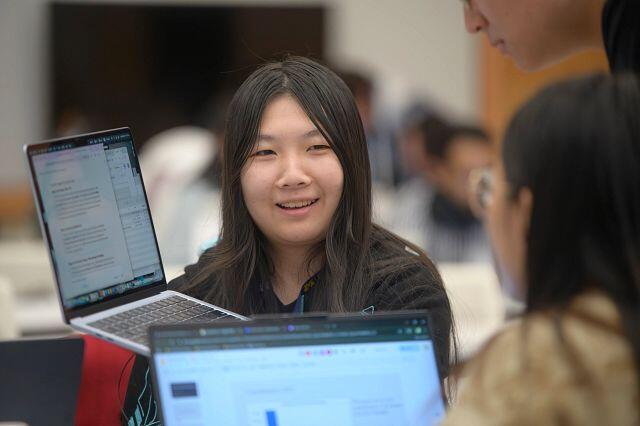 A student holding up a laptop to show someone the screen.