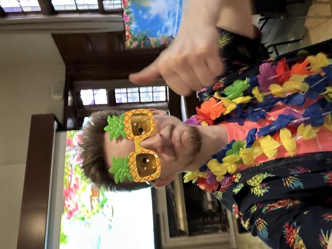 Lance Negrut wearing pineapple sunglasses and a colorful lei and giving a thumbs up to the camera
