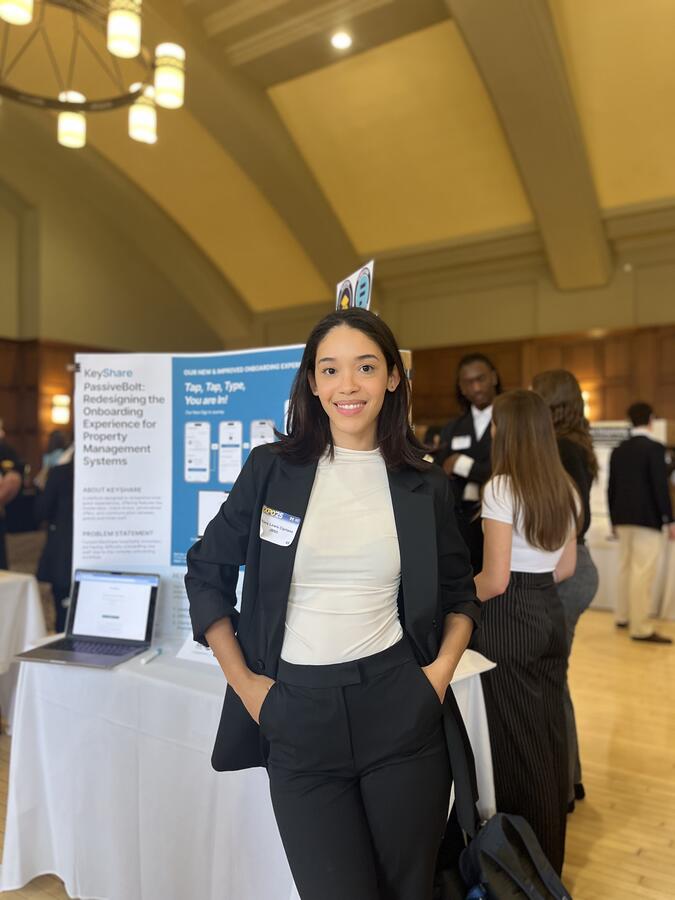 Maiara Lewis-Cipriano posing in front of a research poster in a ballroom.