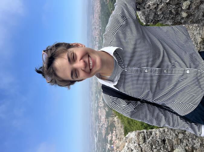 Tessa Kipke smiling at an overlook with trees and a town far away in the background.