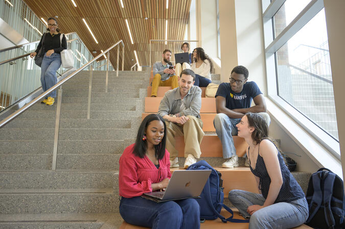 Students sitting on a staircase, chatting and looking at laptops